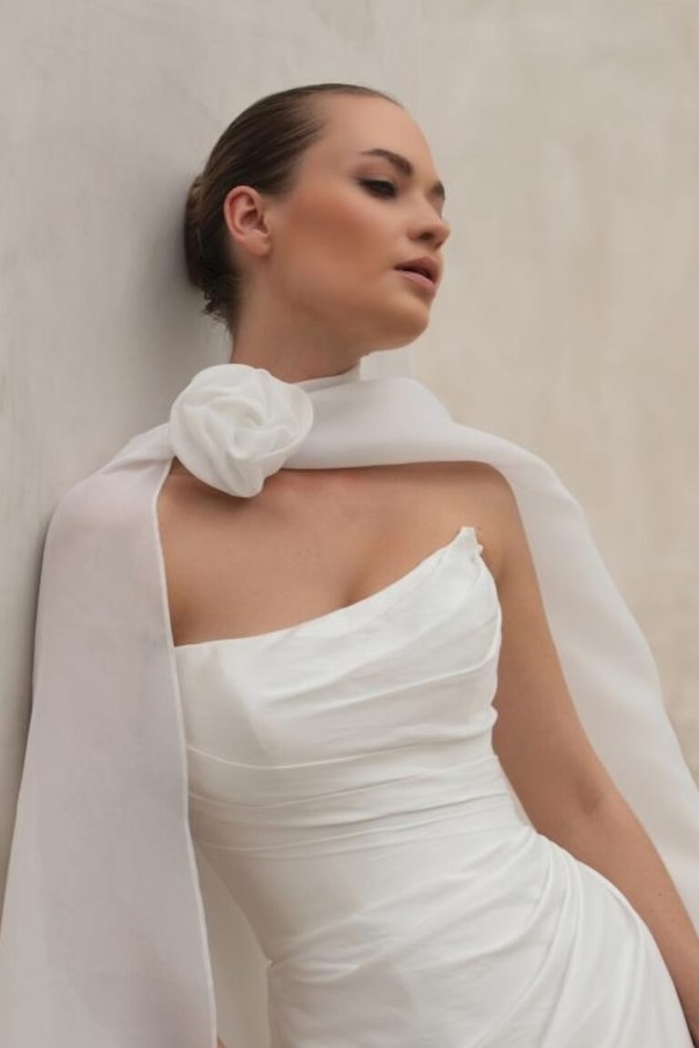 A bride wearing a white cape with a flower in a wedding dress