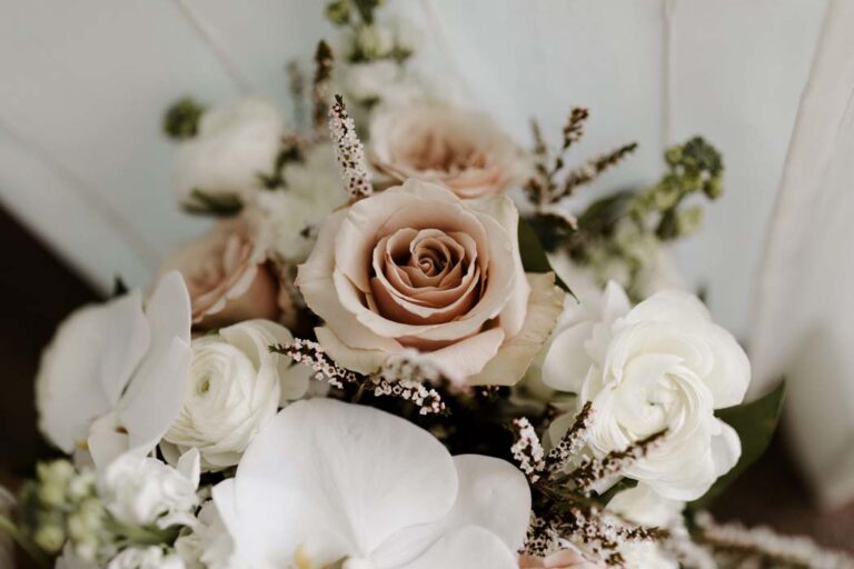 a beautiful wedding bouquet featuring white and blush roses, arranged elegantly with lush green leaves