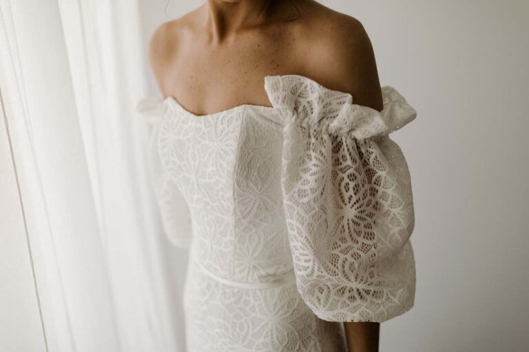 the bride in an off-shoulder lace wedding dress against a white background