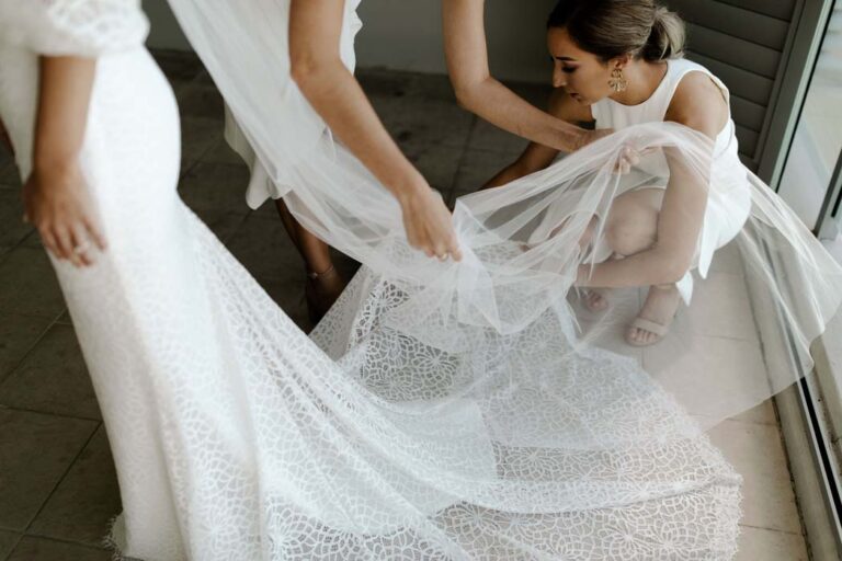 Bride in lace dress with a bridesmaid adjusting her long, sheer veil