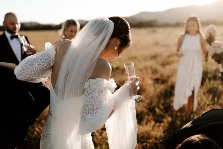the bride and groom stand in a field surrounded by their joyful wedding party, celebrating their special day together