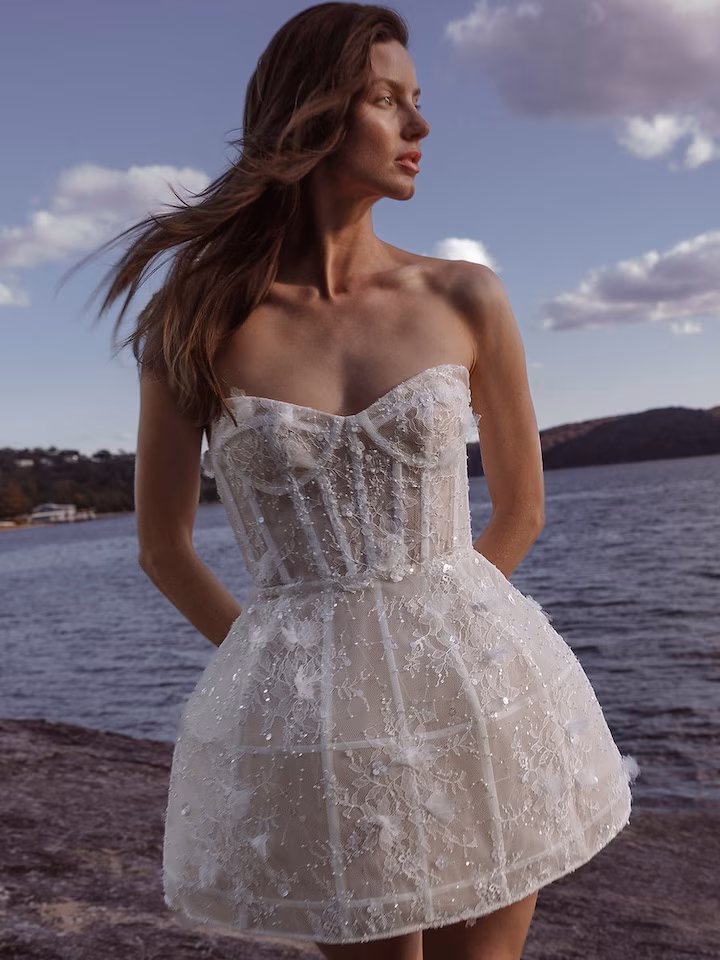 A bride in a mini wedding dress by Aston Bridal, standing by the ocean