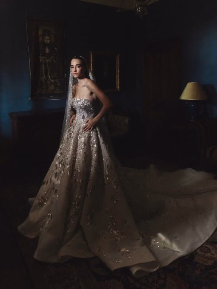 A bride wearing a traditional wedding dress that's embellished with leaves, in a dark room