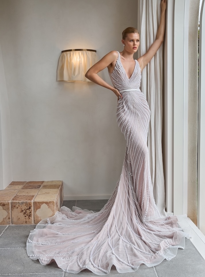 A bride in an embellished wedding gown by Steven Khalil, posing next to a window.