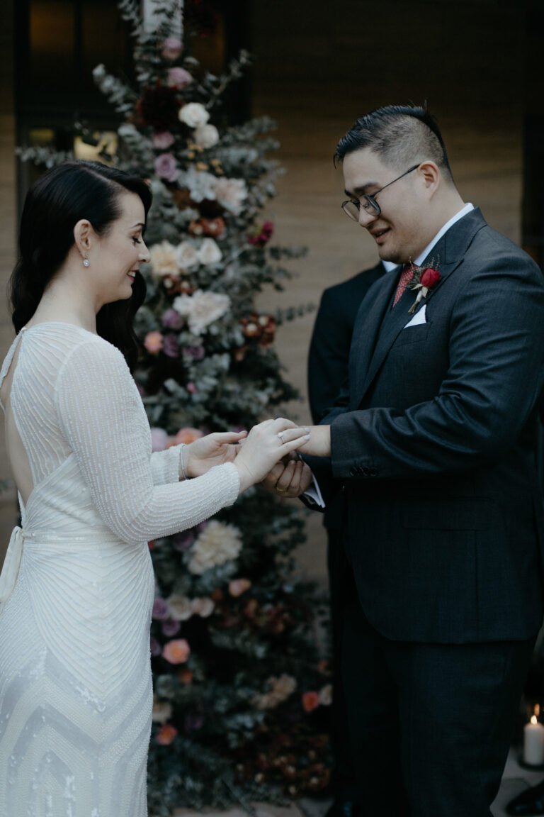 the bride and groom holding hands beside a flower-adorned tree.