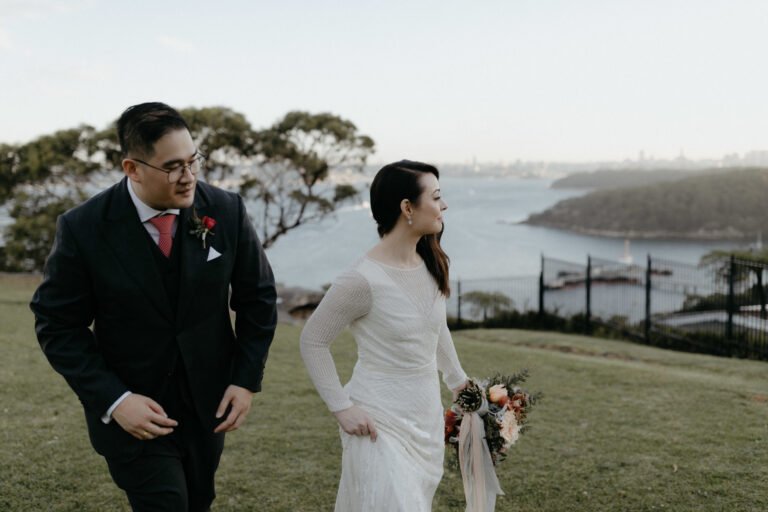 a bride and groom stroll hand in hand down a grassy hill, surrounded by nature on their wedding day