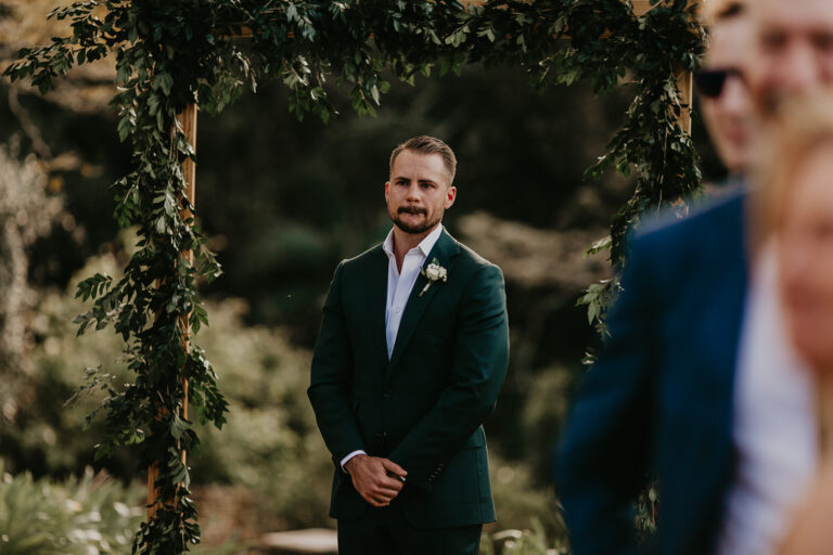the groom at their wedding waiting and watching her bride walking on the aisle