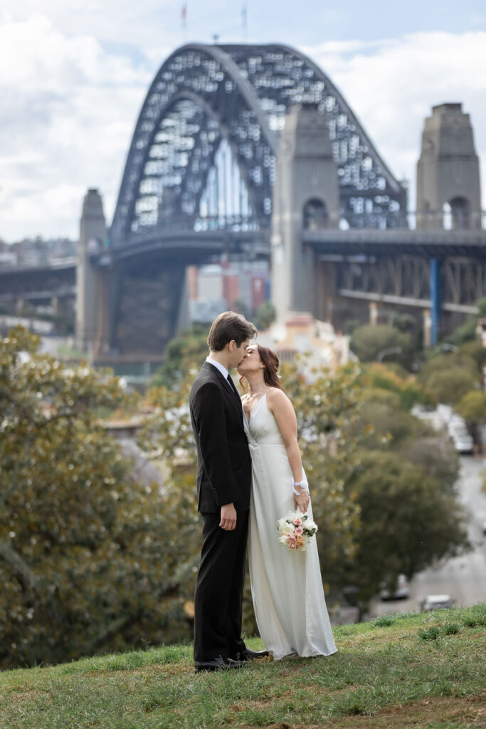 Newly married couple kissing with the Sydney Harbour Bridge on the background captured by wedding photographers in Sydney Australia