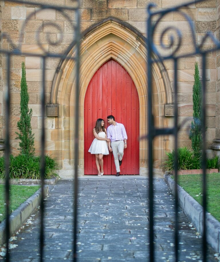 A couple standing in front of a red church door, photographed through the gates