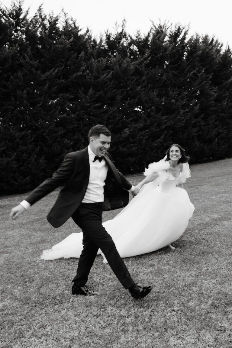a wedding couple running through a grassy area