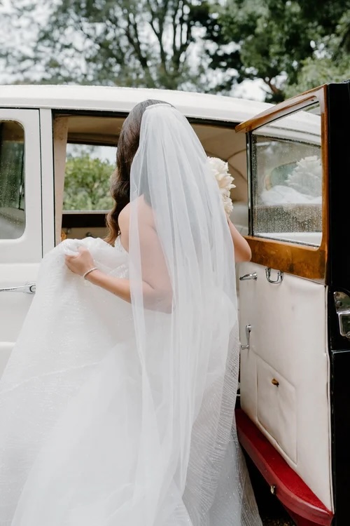 A bride with a veil on getting into a car, photographed from behind by a Sydney wedding photographer