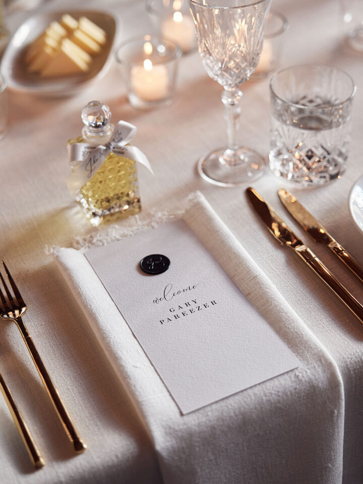 Elegant wedding table setting with menu placed on fine tableware, gold cutlery, and romantic candles.