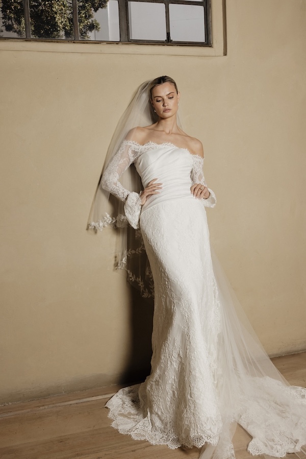 A bride in a long sleeve wedding dress leaning against a wall