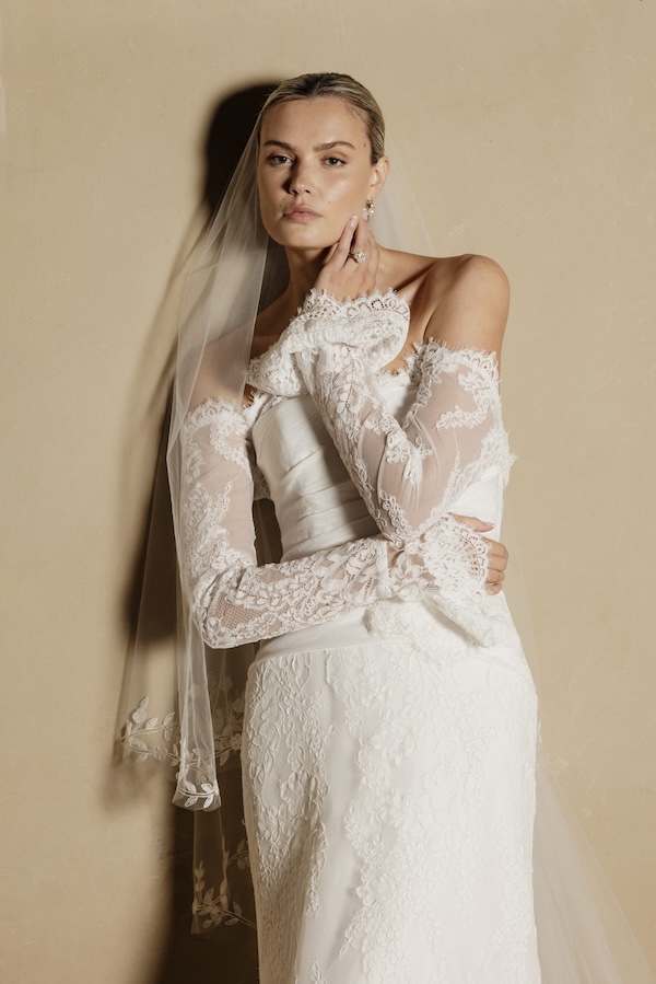 A bride wearing a long sleeve wedding dress looking to camera