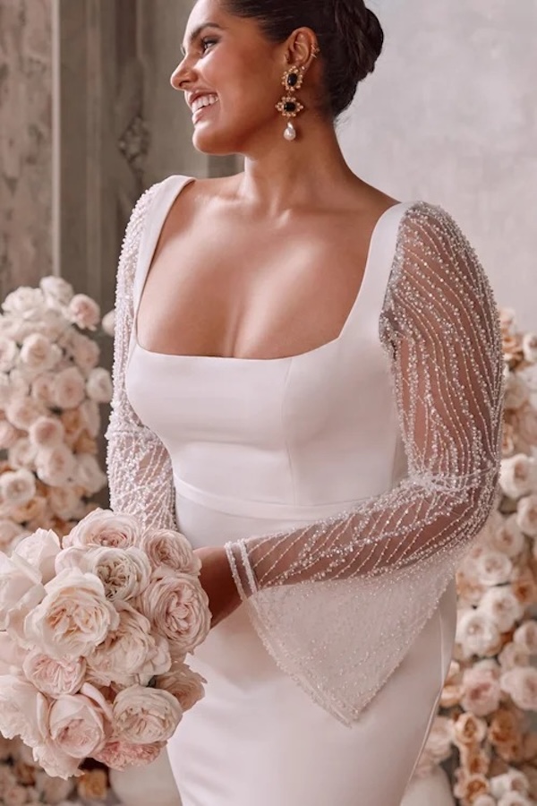 a bride wearing a sheer long sleeve wedding dress, smiling off camera