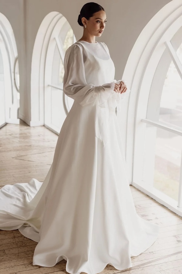 A bride in a modest long sleeve wedding gown with a high neck and sheer sleeves