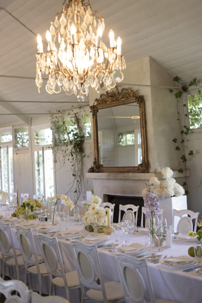 A long table with white linens and a chandelier hanging above it.