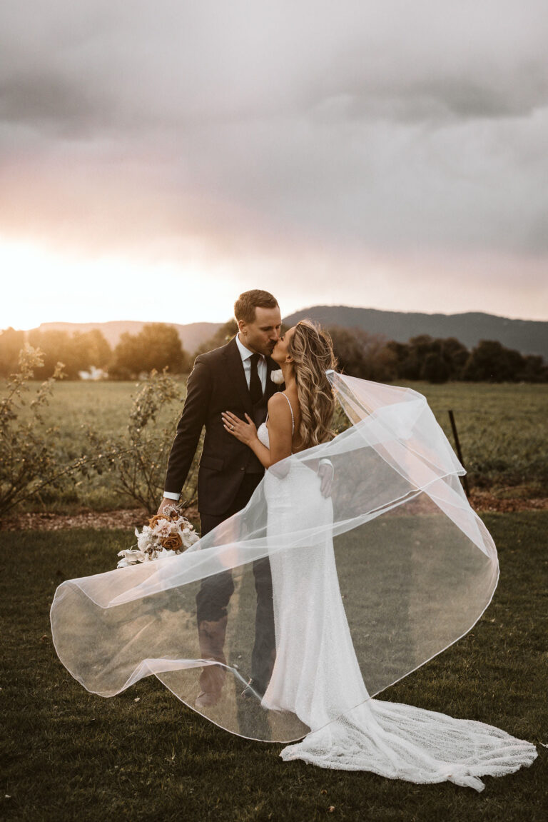 After their wedding Ariana and Tom share a kiss in front of a field during sunset.
