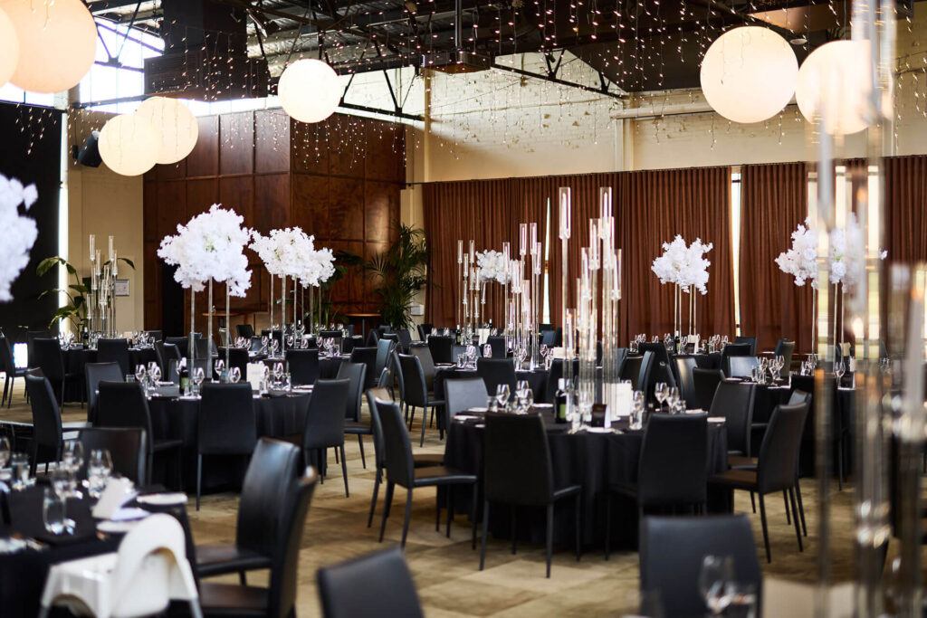 Wedding reception banquet room at Lakeside Pavilion, the best wedding venue in Melbourne, with black tables, white flowers, and black chairs.