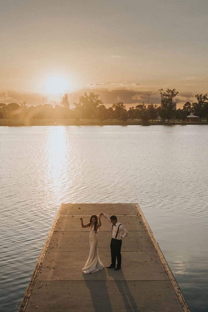 Bride and groom share a dockside dance at Lakeside Pavilion as the lake reflects sunset colours at the best wedding venue in Melbourne.