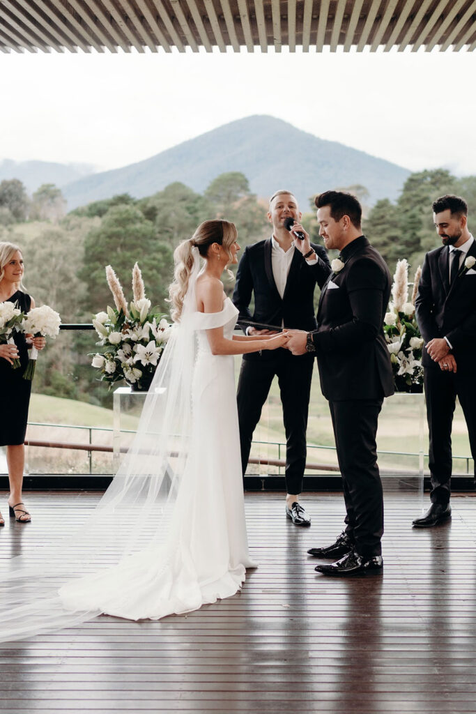 Outdoor wedding ceremony with a Melbourne wedding celebrant guiding the bride and groom as they say their vows, with bridesmaids and groomsmen smiling.