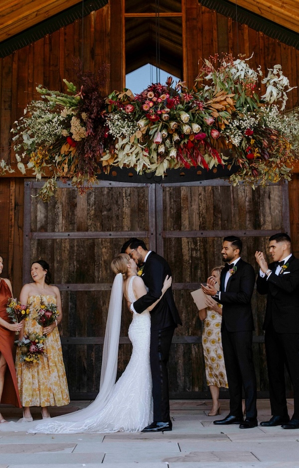 A couple getting married in a wooden panelled venue under a floral display