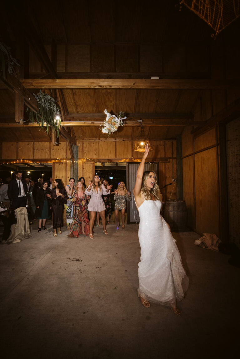 A bride joyfully tosses a bouquet of flowers into the air at a wedding celebration.
