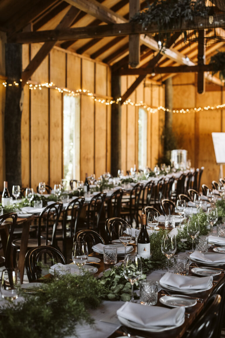 A cozy barn decorated for a wedding reception with string lights, wooden tables, and wildflower centerpieces.