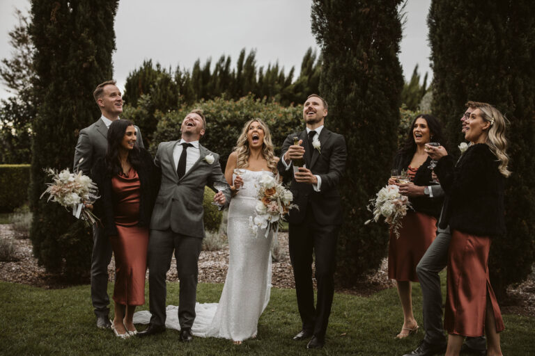 A wedding party smiling in front of trees, celebrating love and happiness.