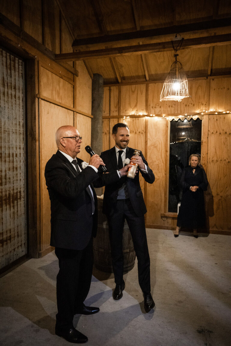 Two men in suits standing in a barn with a microphone.