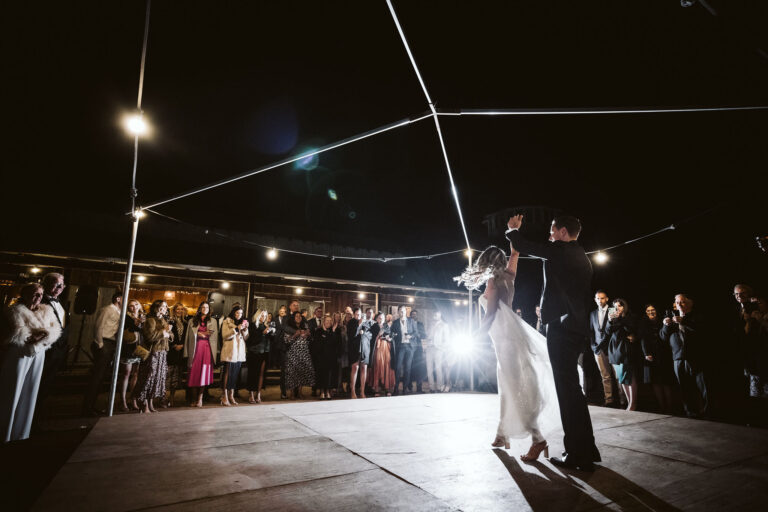 The newlyweds dancing on a stage and the guests watching them.