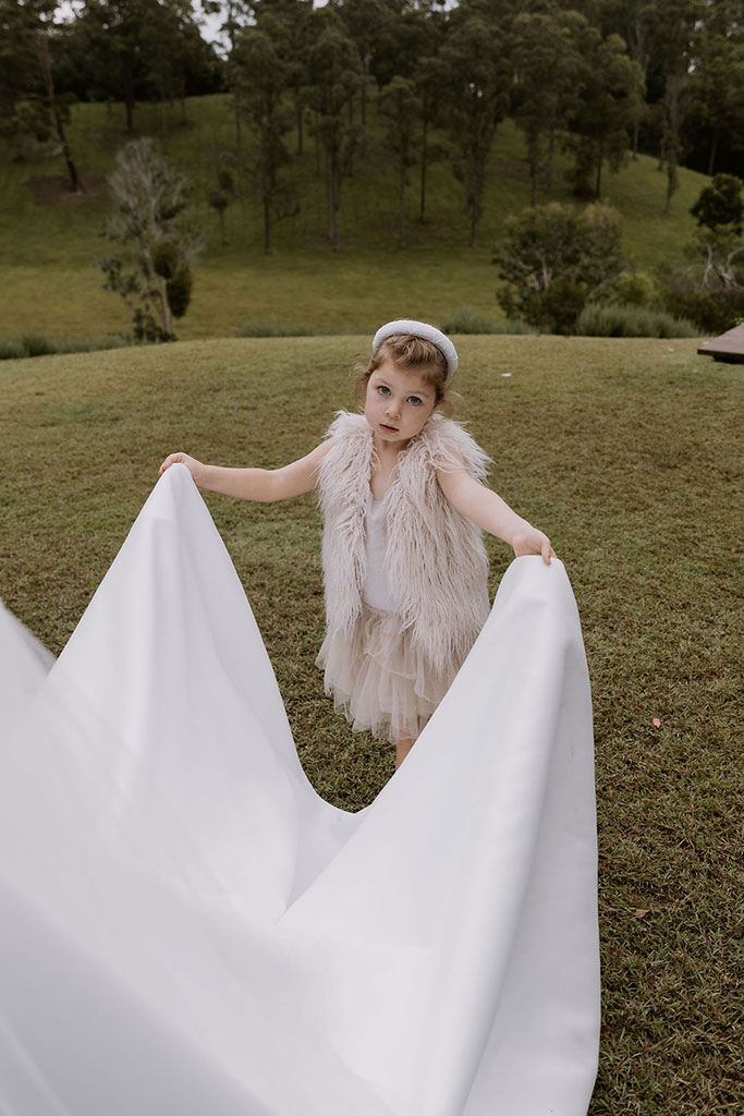 A young girl in a white dress holding the end of the wedding dress.