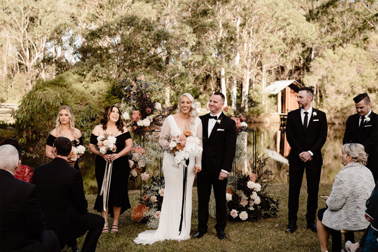 A beautiful outdoor wedding ceremony by the lake, with the bride and groom under a floral arch.