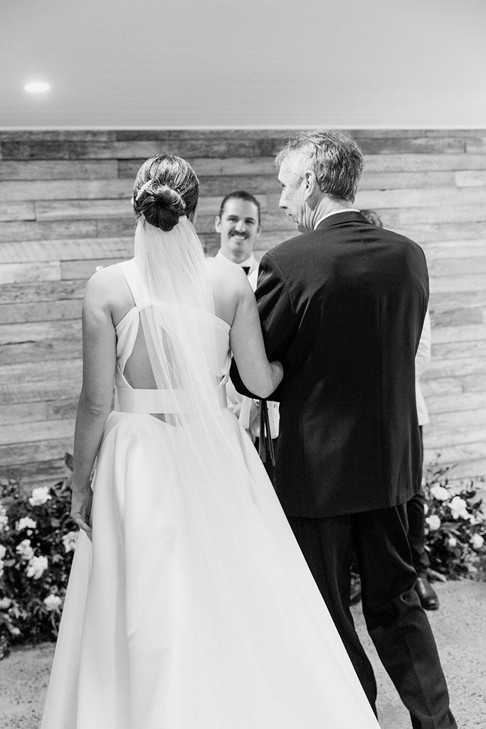 A bride and her father walking down the aisle in a black and white photo.