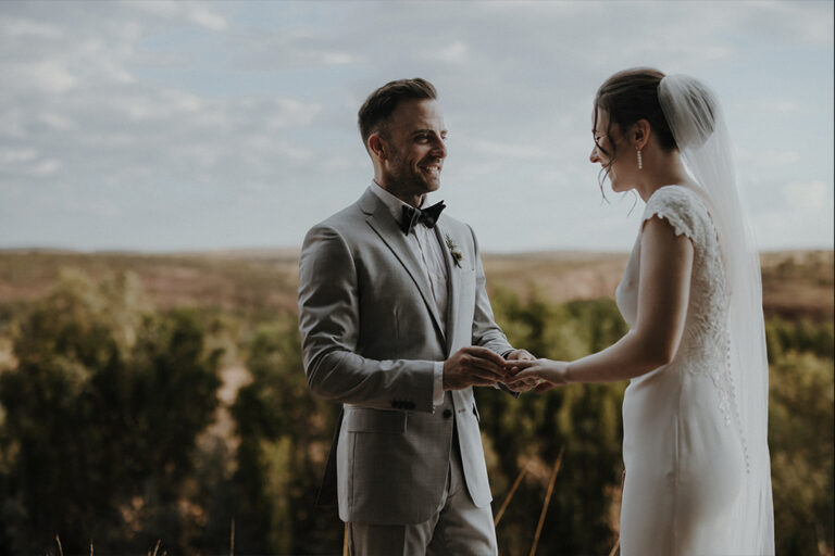 A groom putting a wedding ring on his brides finger.
