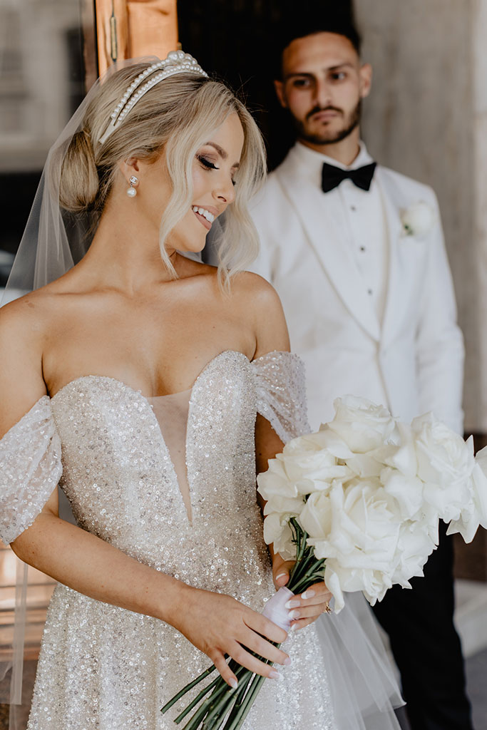 A groom looking at his bride holding a small bouquet of flowers.