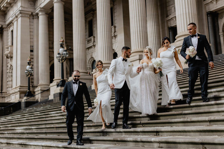 A wedding party descending the steps of the state parliament building, filled with joy and elegance.