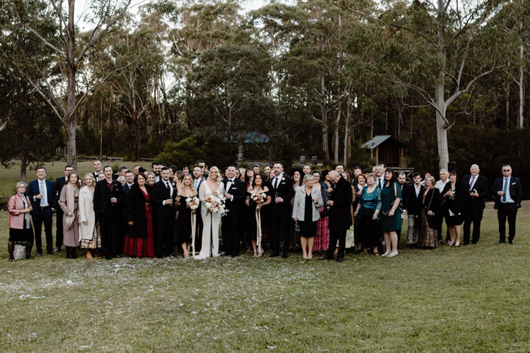 A wedding party smiling for a photo in front of trees.