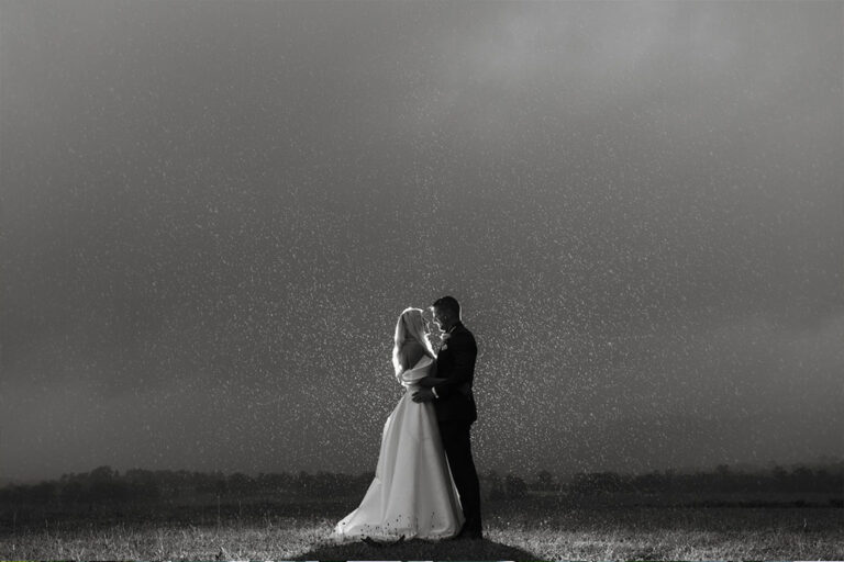 A romantic black and white photo of a bride and groom sharing a kiss in the rain.