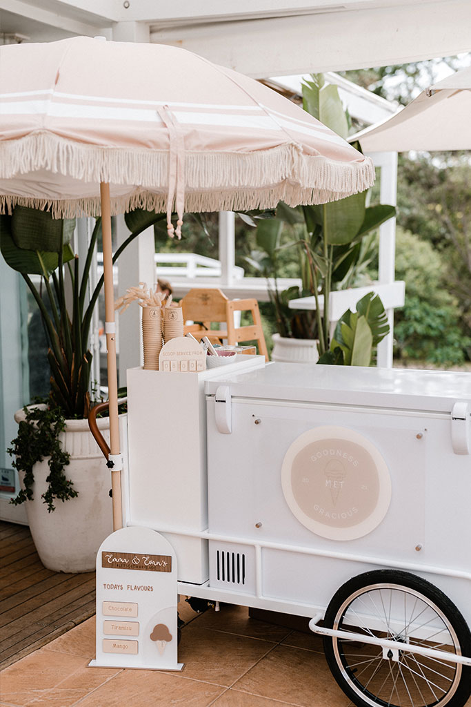 A white ice cream cart with a colorful umbrella on top.