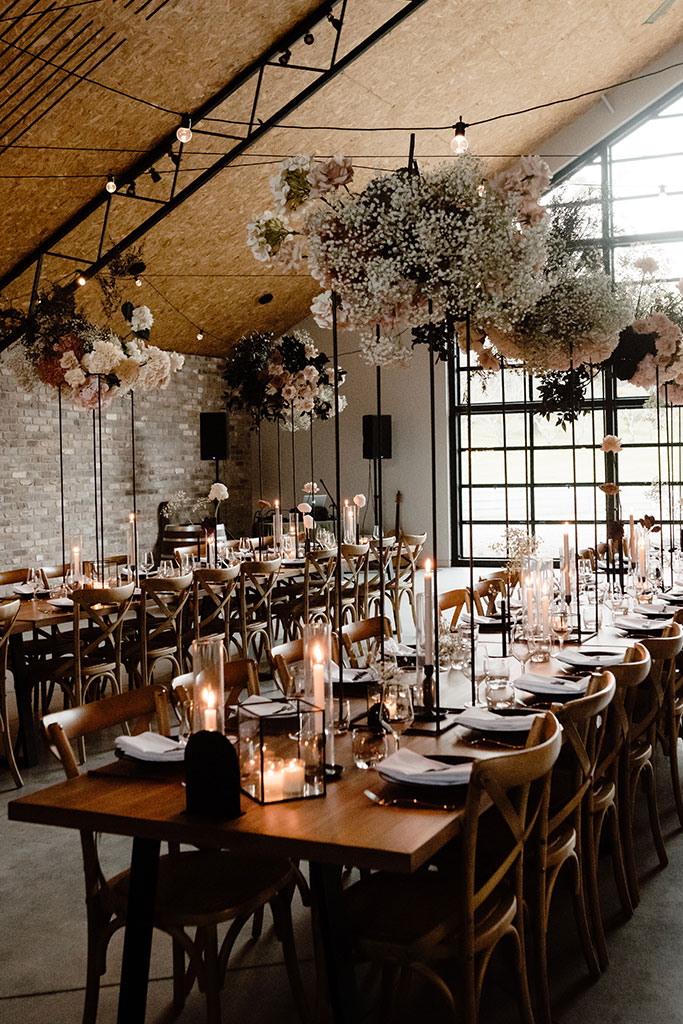 A rustic wedding reception in a barn with wooden tables and chairs.