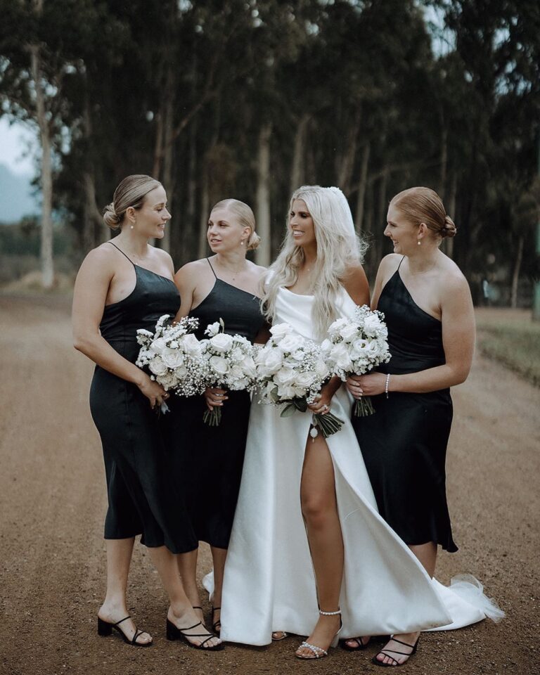 The bride wearing a white wedding dress, and three bridesmaids wearing black wedding gowns beside her.