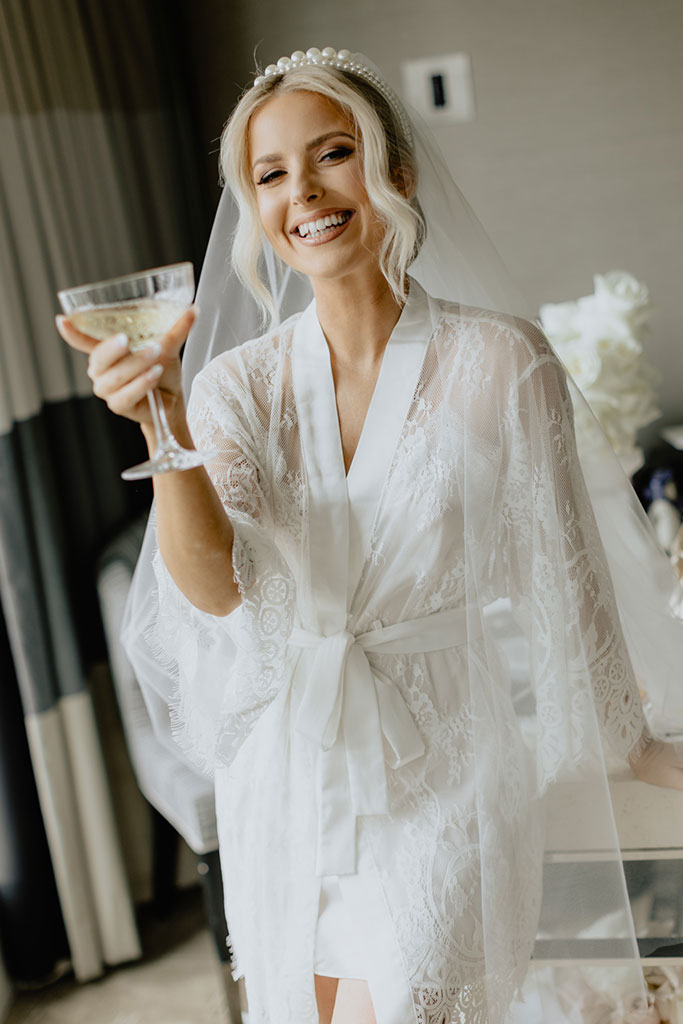 A bride wearing her wedding gown and holding a glass of champagne.