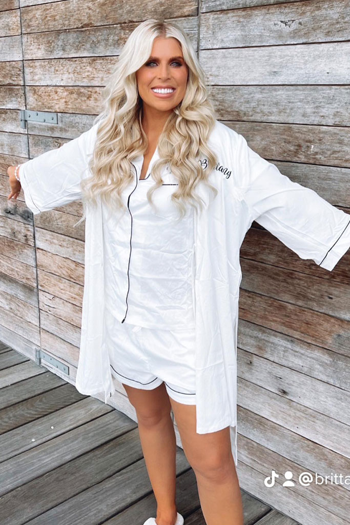 A blonde woman in white pajamas and shorts, smiling.