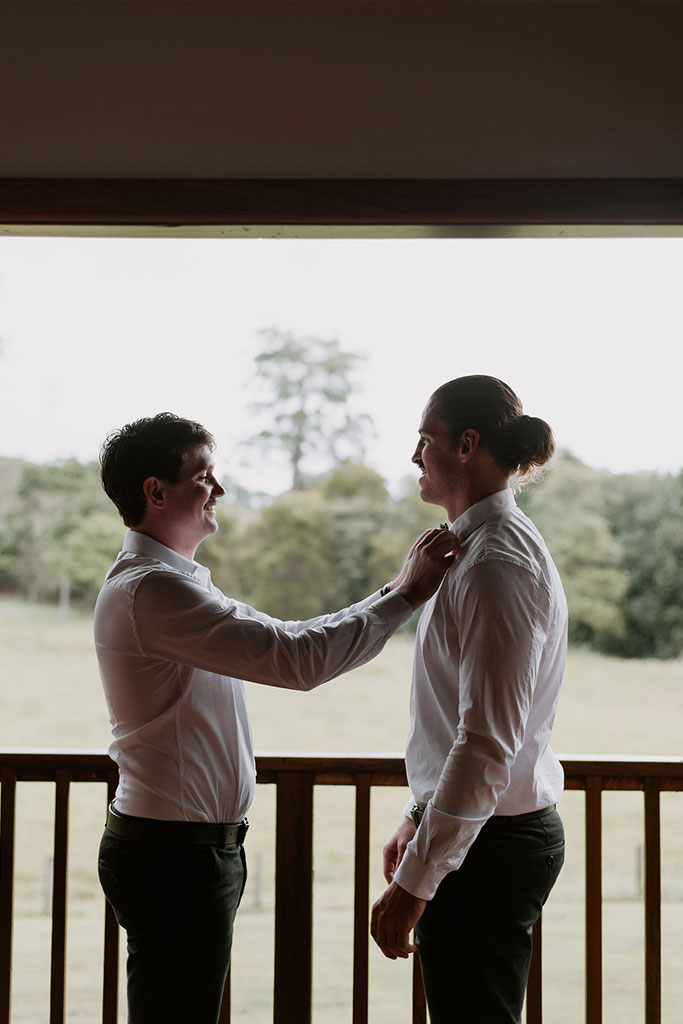 Two men in white shirts and ties helping each other adjust their ties.