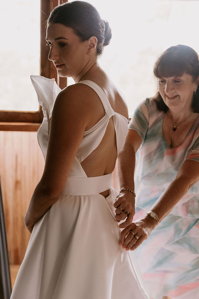 A woman assisting another woman in putting on her wedding dress.