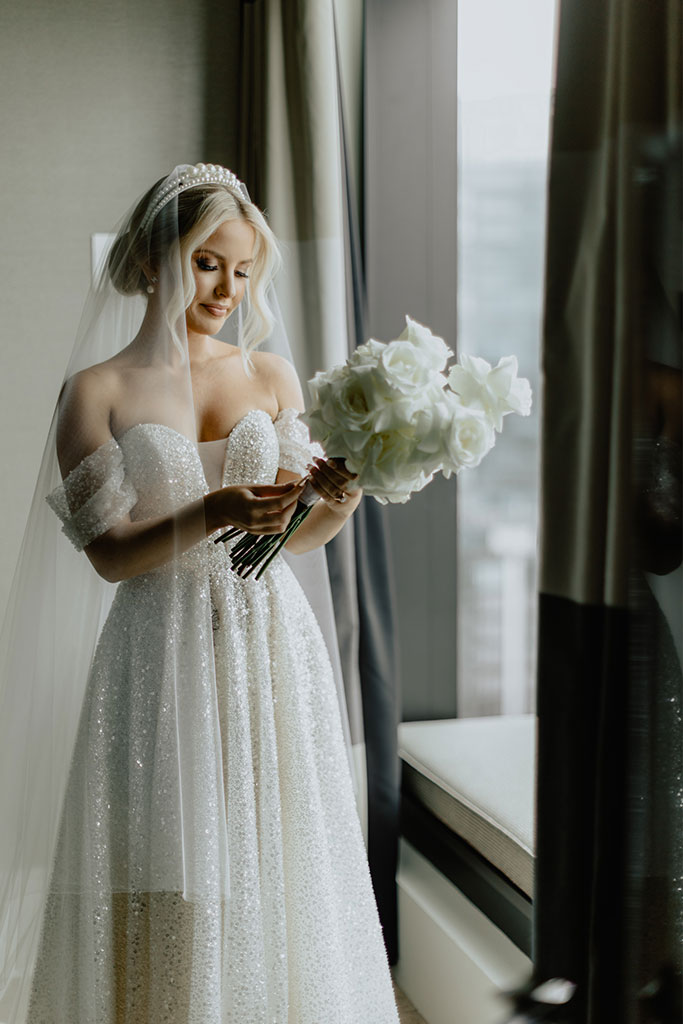 A bride in a white wedding dress admiring her bouquet of flowers.