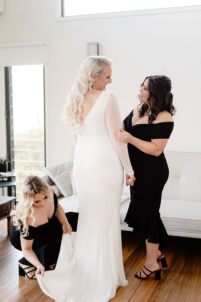 Two women wearing black gowns fixing the brides wedding dress.