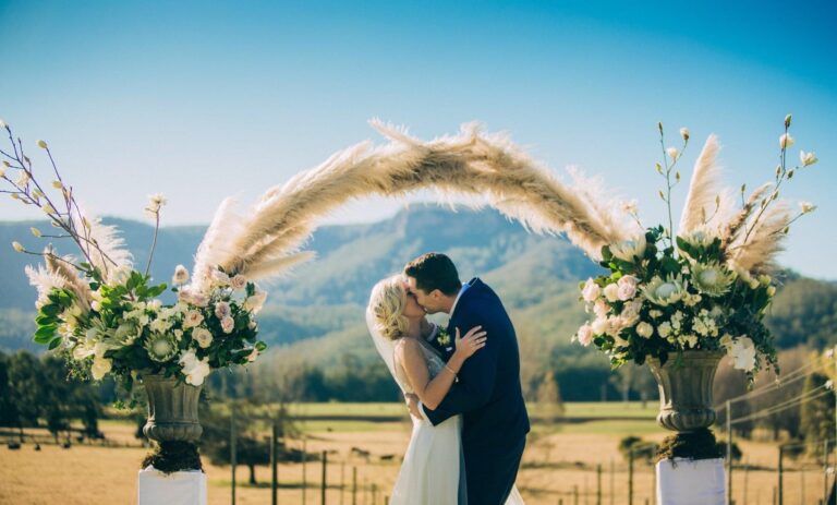 A bride and groom share a kiss under a mountainous arch.