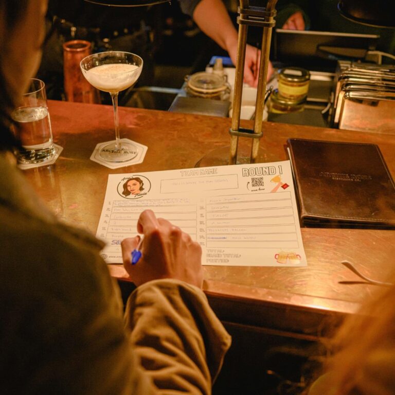 A person sitting at a bar with a drink filling up a form.